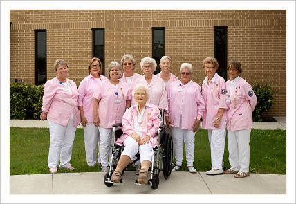 This picture is of 10 elderly ladies all wearing pink tops with white pants, one of the ladies is in a wheelchair in front of the other ladies
