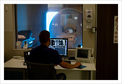This is a picture of a Nurse or doctor sitting in a room where the imagines are being processed from the MRI through the window of the next room